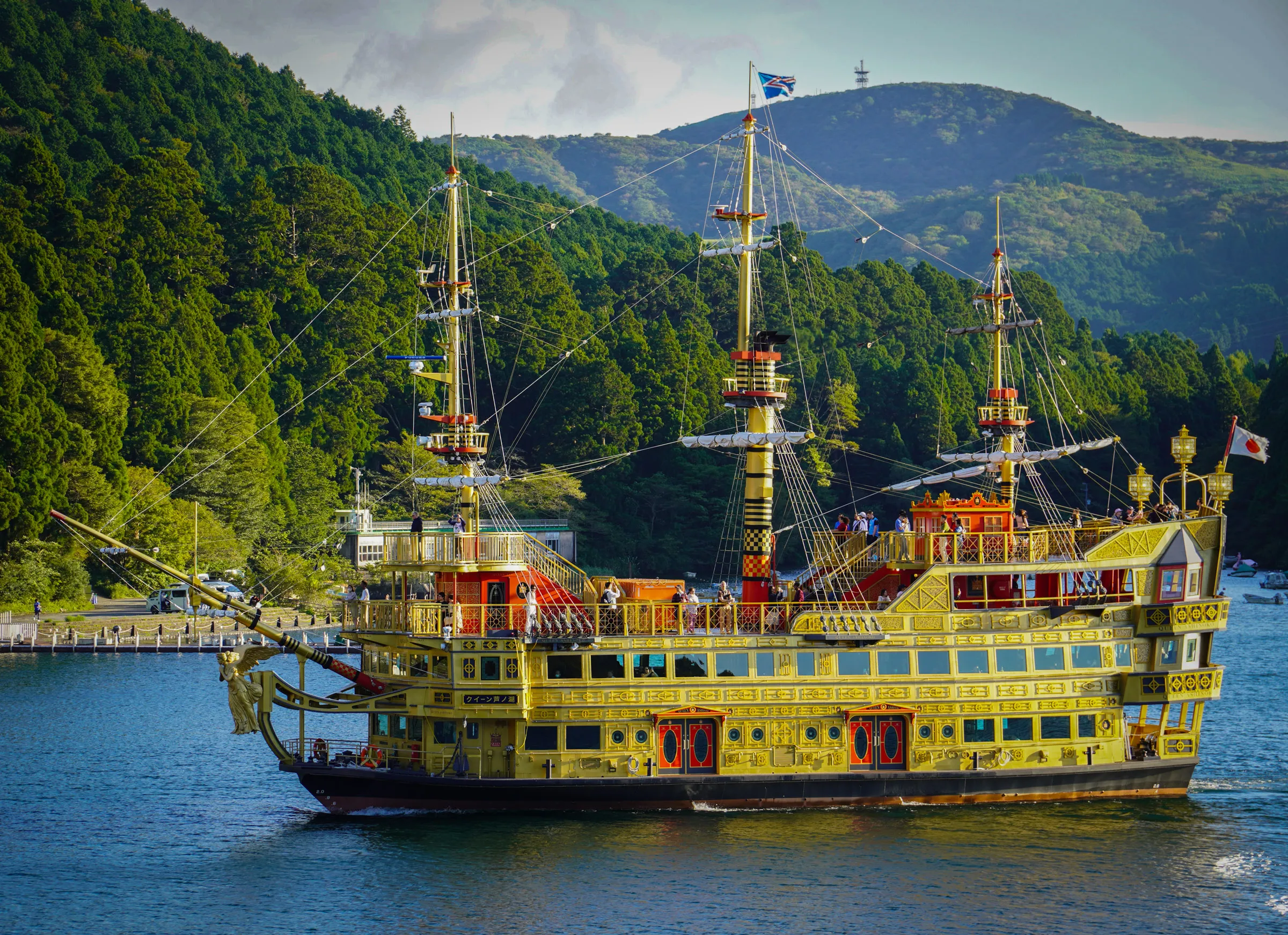 An ornate gold pirate-ship-style tour boat with red trim and rigged masts crossing Lake Ashi, forested hills behind it