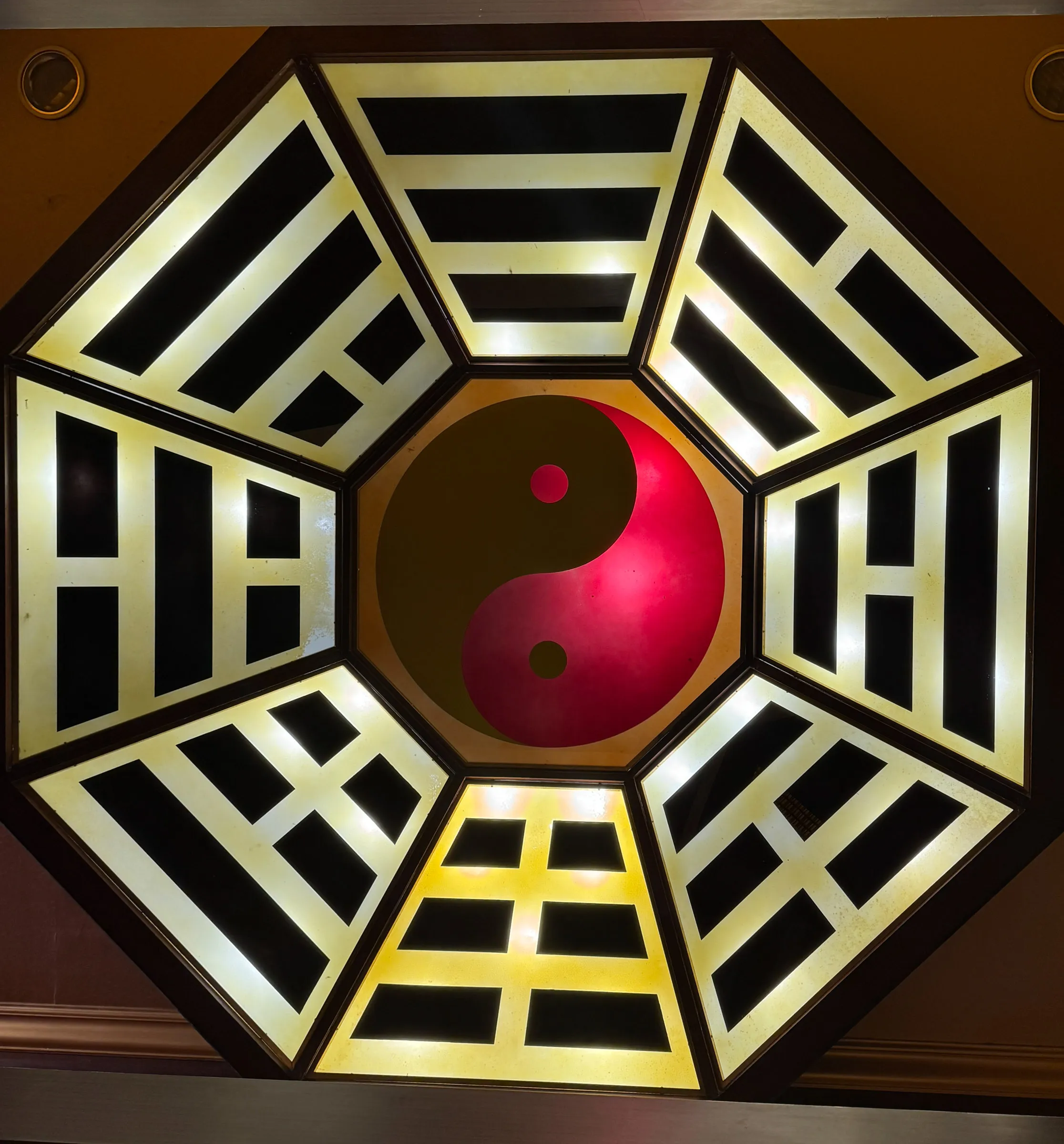 An octagonal skylight patterned with the eight trigrams in black and gold, glowing around a red and gold yin-yang symbol at its centre